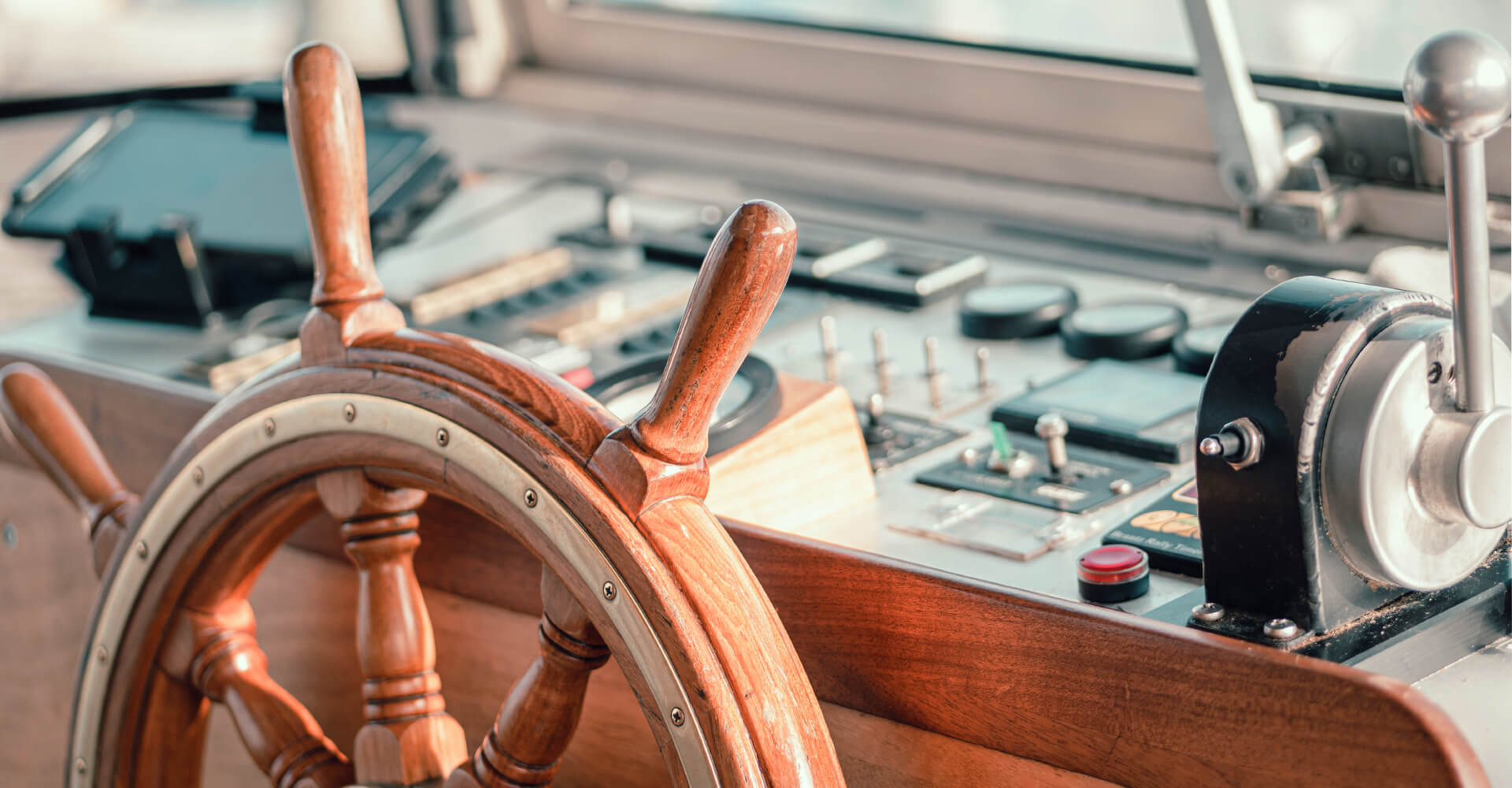 Nahaufnahme eines hölzernen Steuerrads und eines Steuerhebels auf einem Bootskontrollpult.